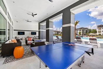 A blue ping pong table is in the middle of a room with a pool table and chairs.